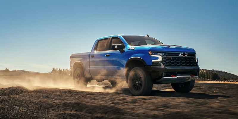 Blue Chevrolet Silverado 1500 driving through the desert kicking up sand